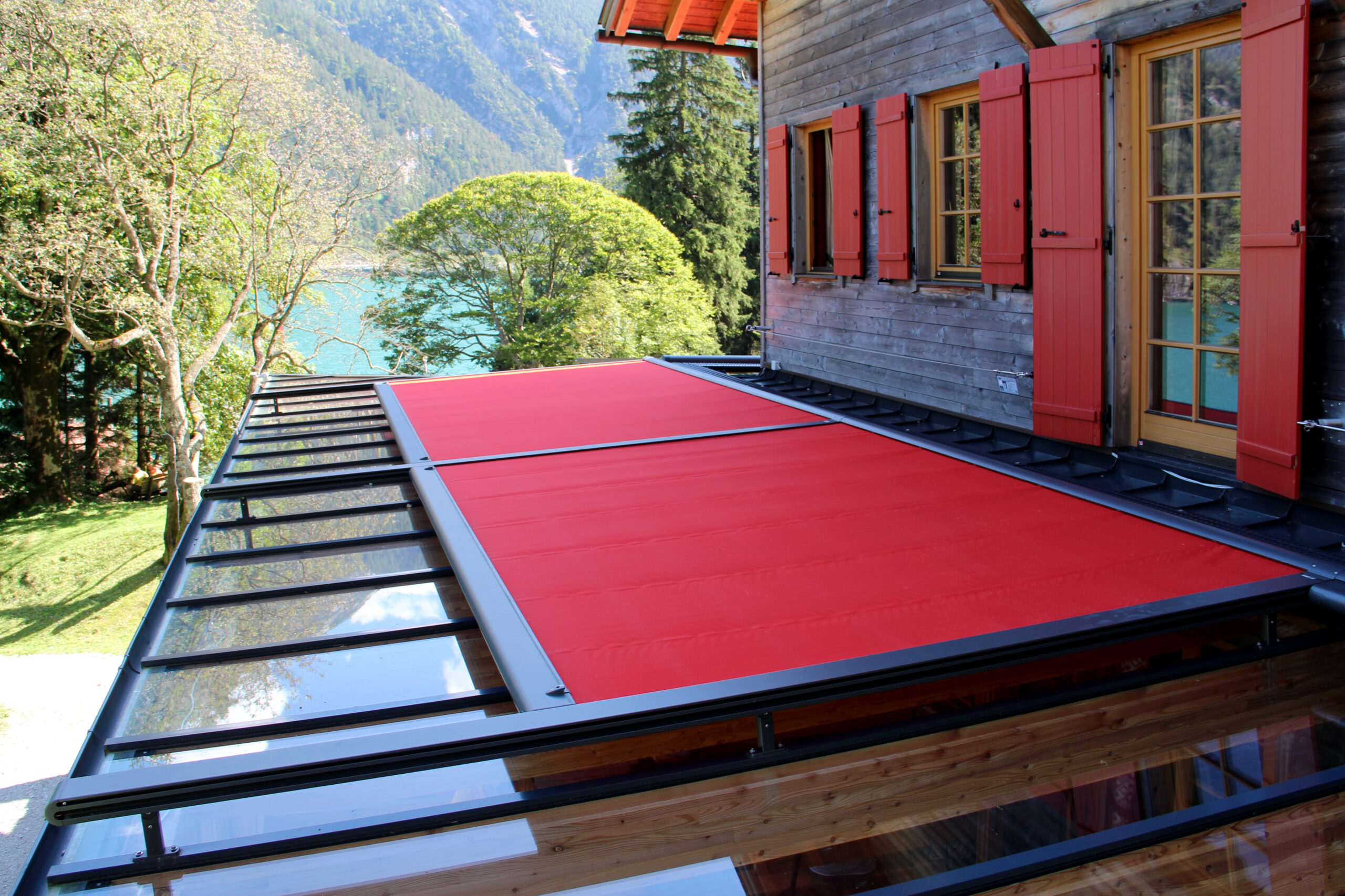 Referentiebeeld bovenste glazen scherm markilux 8800 met rode schermdoek, bovenaanzicht van het doek. Het ontwerp van het scherm past bij het houten huis met rode luiken.