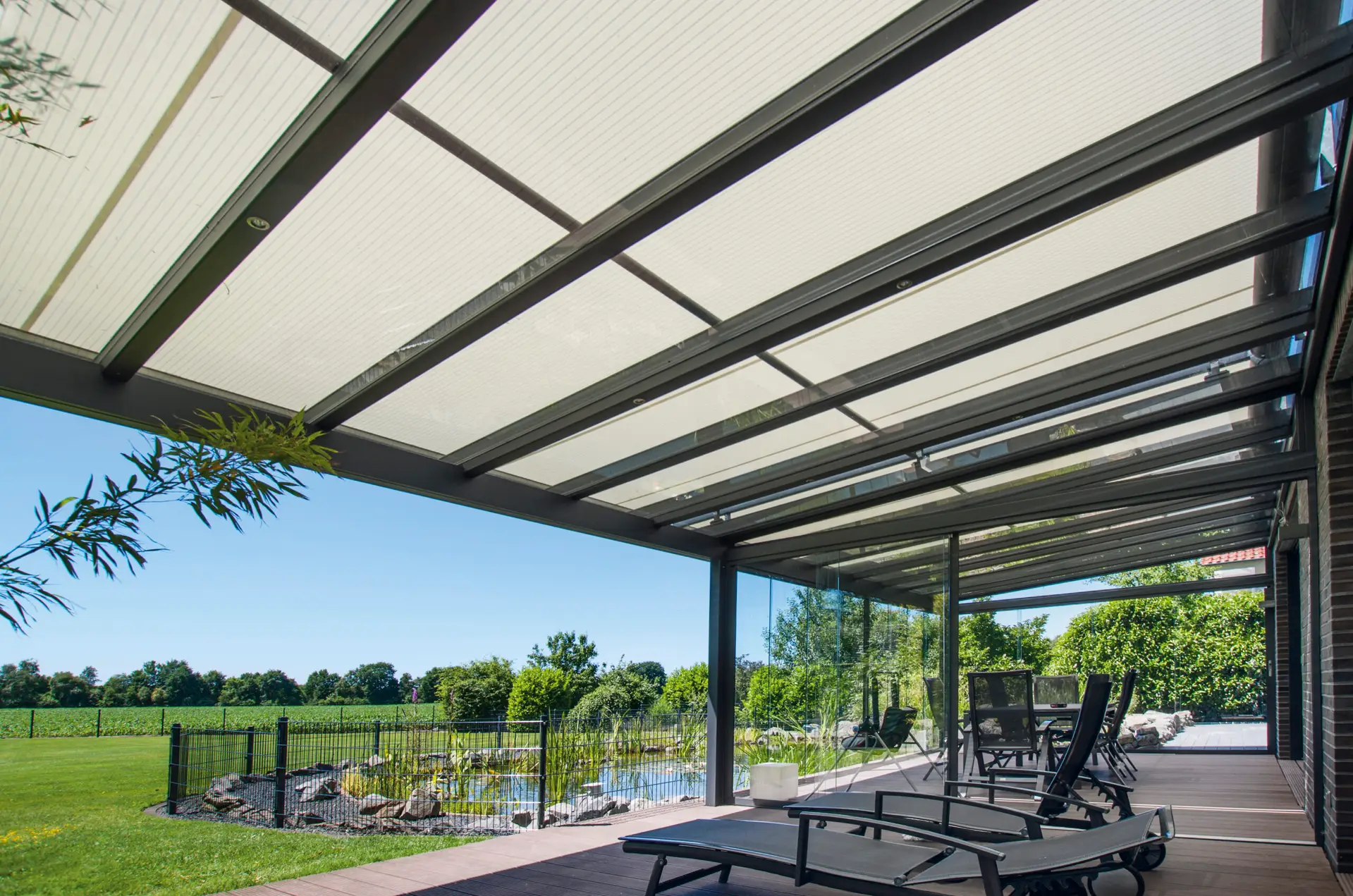 Terrasoverkapping met scherm voor glazen overkapping markilux 8800, zicht onder de overkapping naar buiten naar de tuin met vijver.